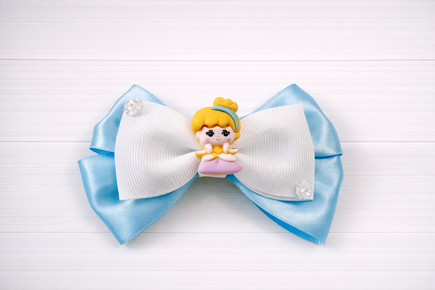 Large blue and white bow with a small Cinderella figurine on a light wooden background