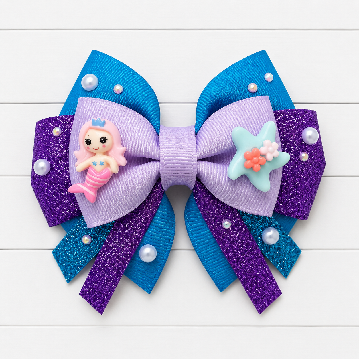 Decorative hair bow with mermaid charm and starfish on a white wooden background
