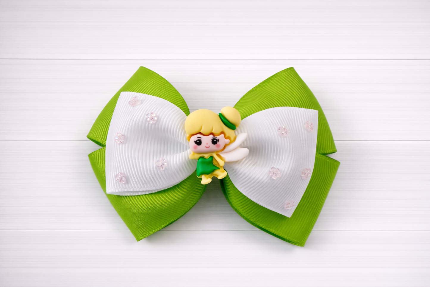 Green and white hair bow with a Tinkerbell charm in the middle on a white wooden background