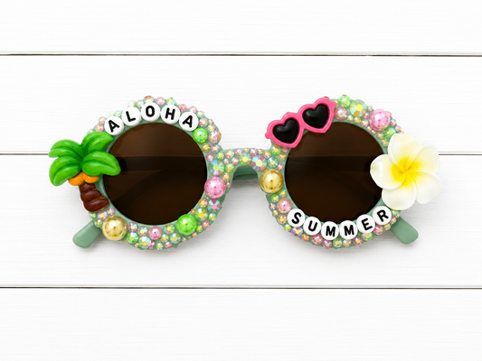 Kids flower green sunglasses with palm tree charm on left and sunglasses and flower charm on right. "ALOHA SUMMER" text outlines frames. Frames decorated with yellow, pink, and green rhinestones and pearls.