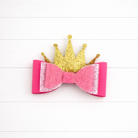 Pink glittery bow with a gold crown on a white wooden background