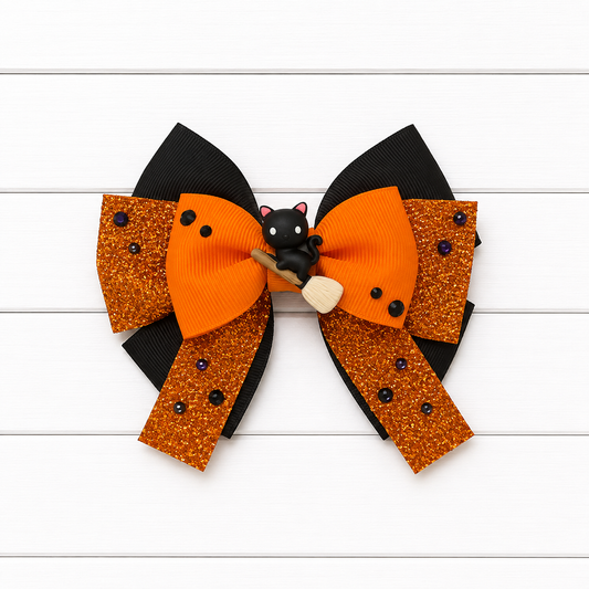A double-layered hair bow featuring orange grosgrain ribbon, orange glitter panels with black bead accents, black ribbon loops, and a small black cat wearing a witch hat on a broomstick at the center, displayed on a white wood plank background.