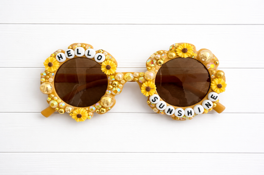 Kids yellow flower sunglasses with sunflower charms, yellow and gold rhinestones and pearls, and 'HELLO SUNSHINE' text outlining frame