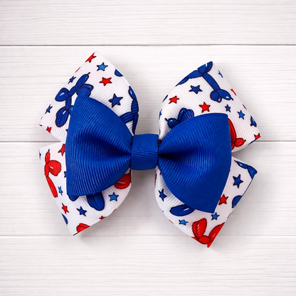Two hair bows with blue centers and red, white, and blue patterns on a white wooden background.
