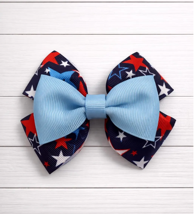 Blue bow with red, white, and blue patterned star bow behind on a white wooden background