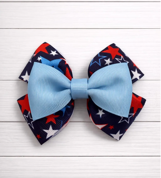 Blue bow with red, white, and blue patterned star bow behind on a white wooden background