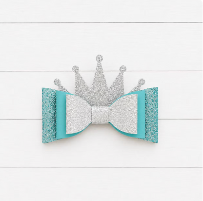 Silver crown and turquoise bow on a white wooden background