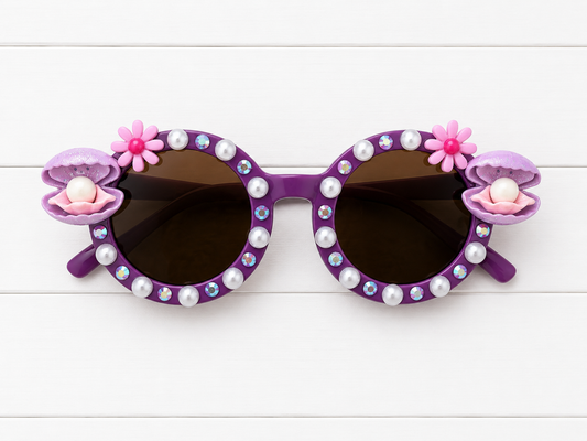 Kids purple round sunglasses with clam charms on both sides and white pearls and rhinestones outlining the frames.