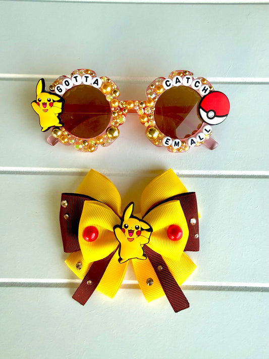 A pair of round novelty sunglasses and a large yellow and brown hair bow, both decorated with Pikachu and Pokémon-themed embellishments, displayed on a white paneled background.