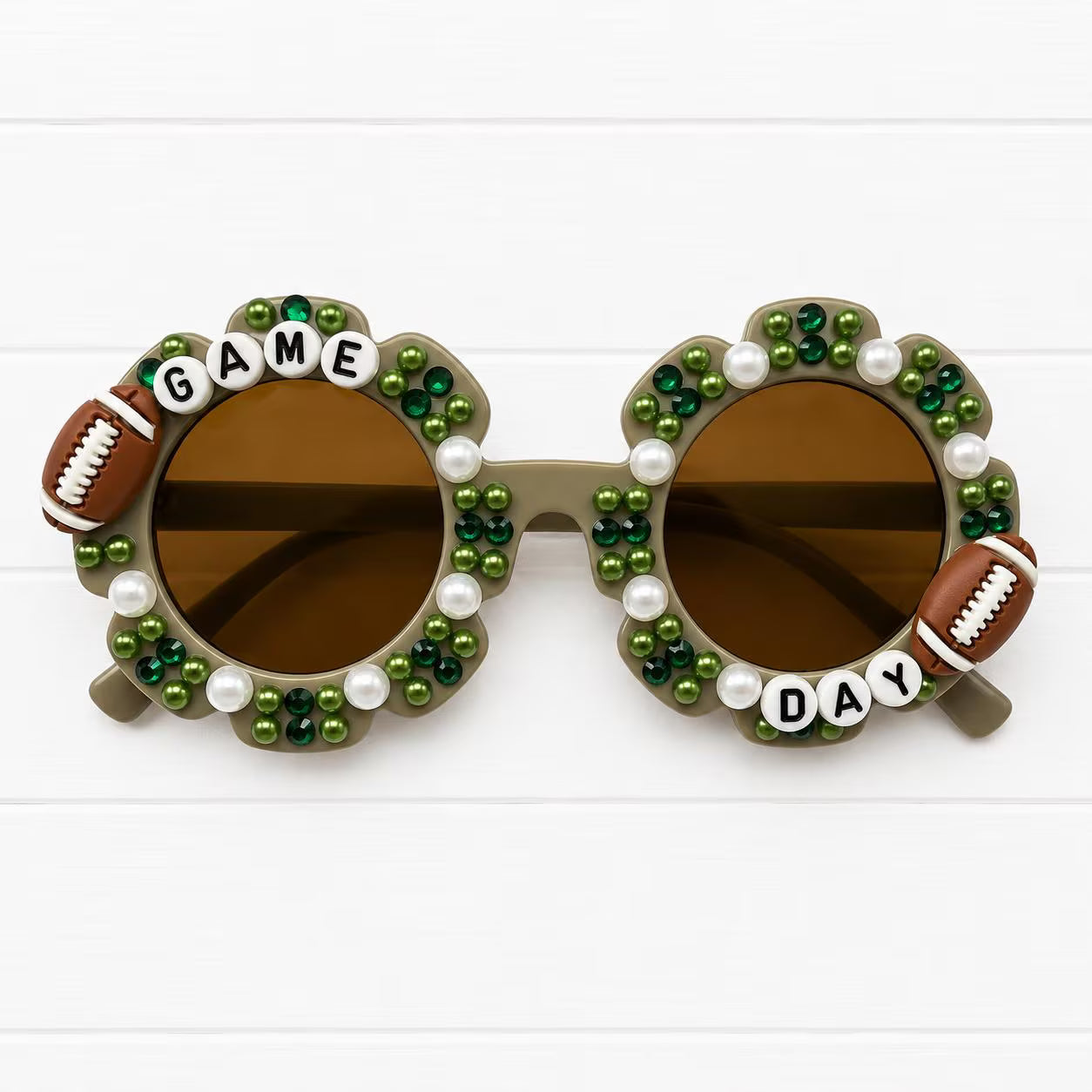 Kids grey flower sunglasses with two football charms and green and white pearls and rhinestones decorating the frames. "GAME DAY" text outlines the frames.