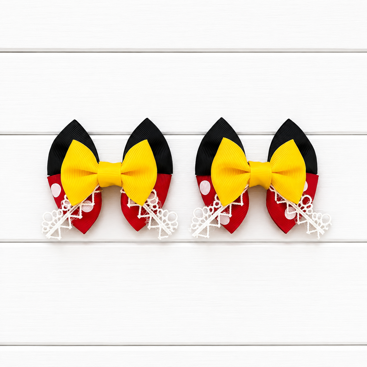 Two matching hair bows styled like the Minnie Mouse headband, featuring black and red sections with white polka dots and a bright yellow bow, displayed on a white wood plank background.