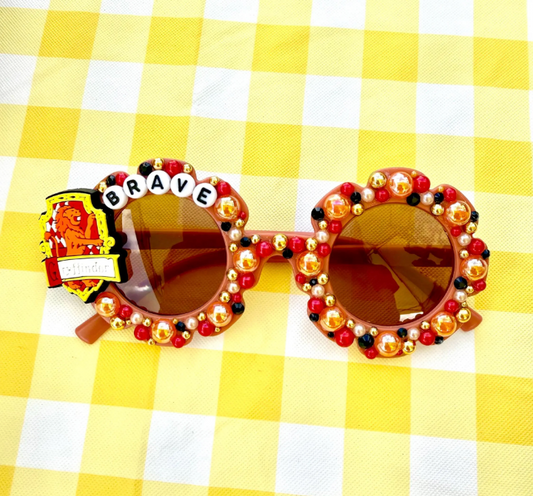 Kids flower burnt red sunglasses with Gryffindor logo on the left and "Brave" text on the frame. There are red, gold, and black rhinestones covering the frames.