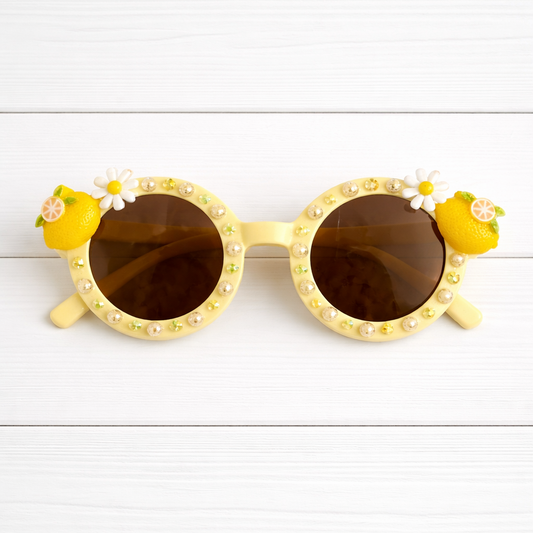 Kids round light yellow sunglasses with lemon charms on the frames and yellow rhinestones and pearls outlining the remainder of the frames.