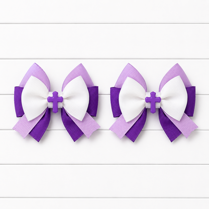 Two matching purple and white ribbon hair bows with a small cross center, displayed side by side on a white wood plank background.