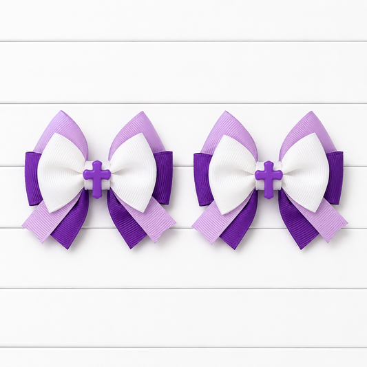 Two matching purple and white ribbon hair bows with a small cross center, displayed side by side on a white wood plank background.