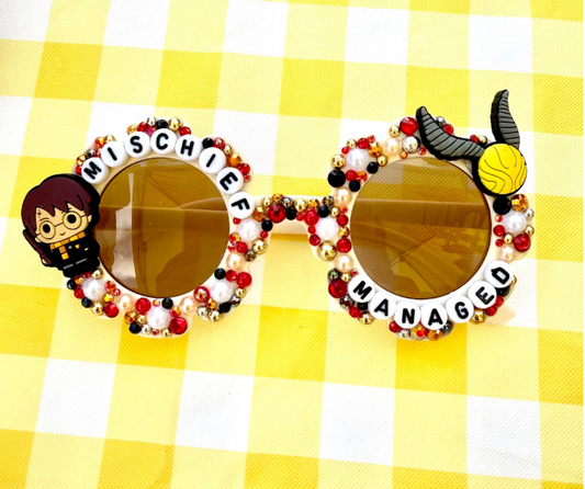 Kids cream flower sunglasses with Harry Potter charm on left and Snitch charm on right. "Mischief Managed" text outlines frames and there are pearl, red, gold, and black rhinestones and pearls covering the frames.