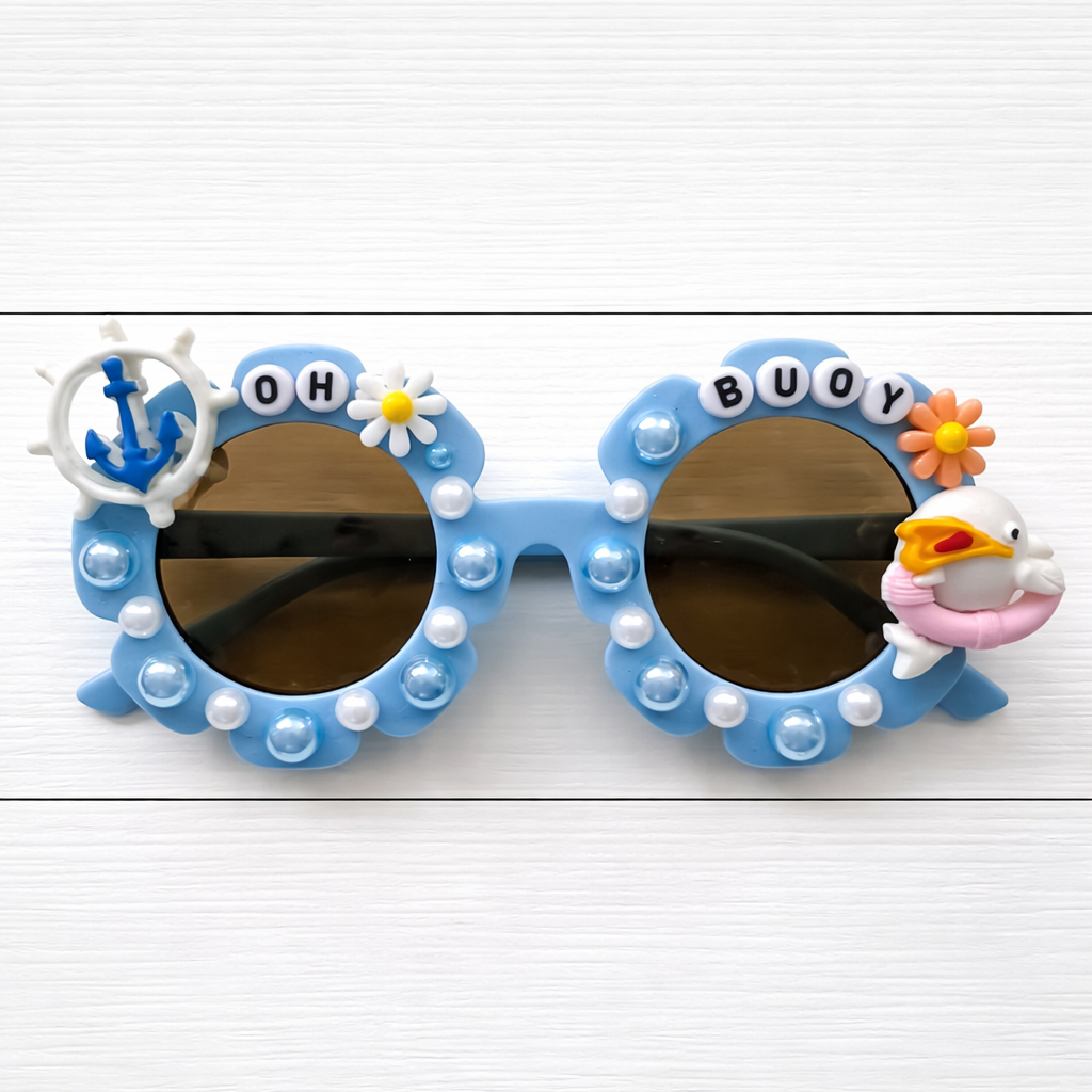 Kids blue flower Sunglasses with blue and white pearl outlined frames featuring anchor charm on left and dolphin charm on right on a white wooden background