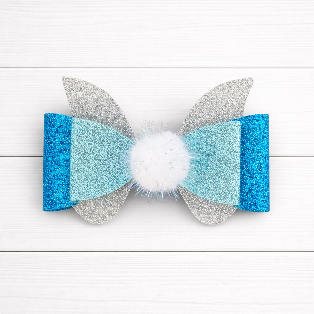 Glittery blue, silver bow with a white pom pom in the middle on a white wooden background
