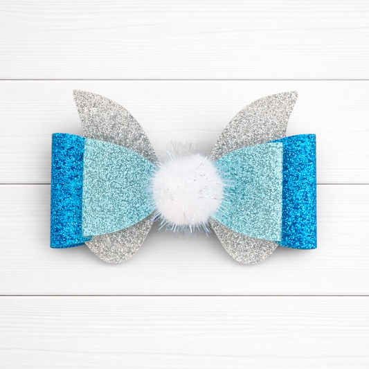 Glittery blue, silver bow with a white pom pom in the middle on a white wooden background