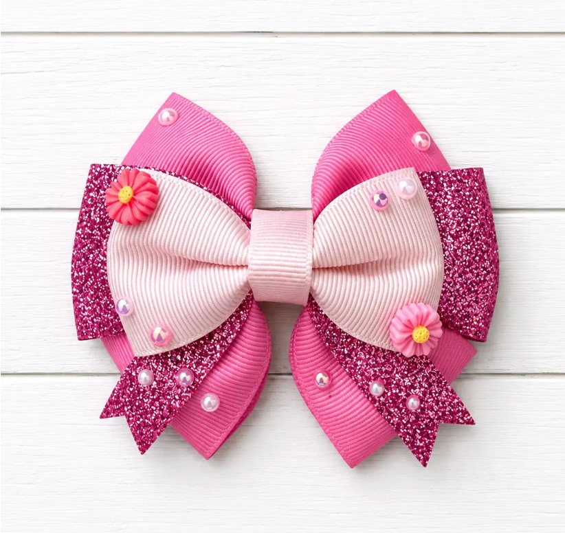 Pink and white decorative bow with flowers and beads on a light wooden background