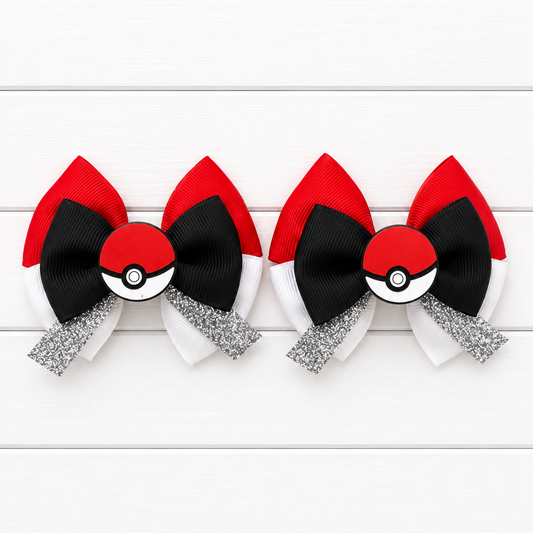 Two matching hair bows styled like Pokémon balls, featuring red and black ribbons, white ribbon sections, and a silver glitter bow, displayed on a white wood plank background.