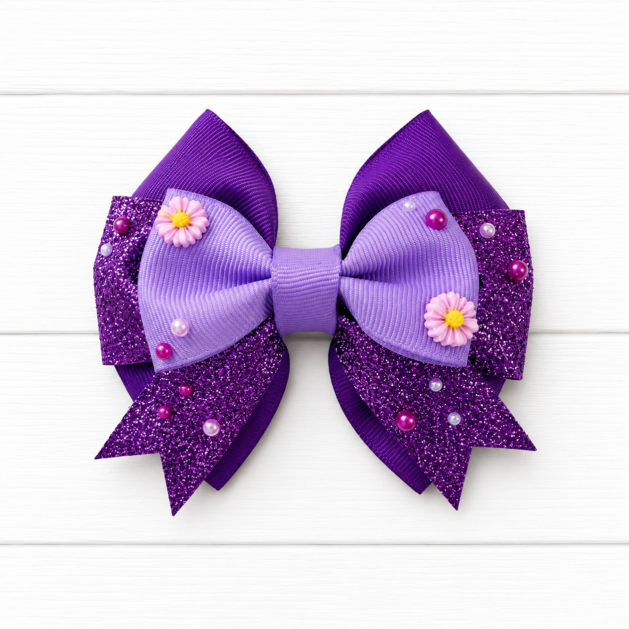 Purple glittery hair bow with purple flowers and beads on a white wooden background