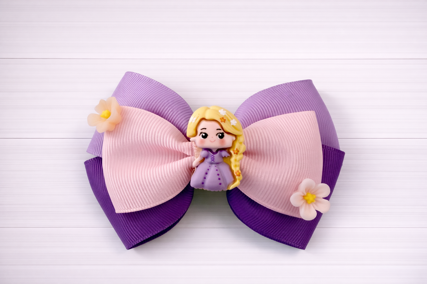 Large hair bow with purple and pink colors, featuring a Rapunzel charm in middle and flowers on the sides.