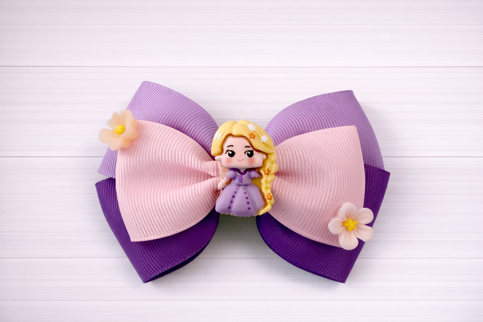 Large hair bow with purple and pink colors, featuring a Rapunzel charm in middle and flowers on the sides.