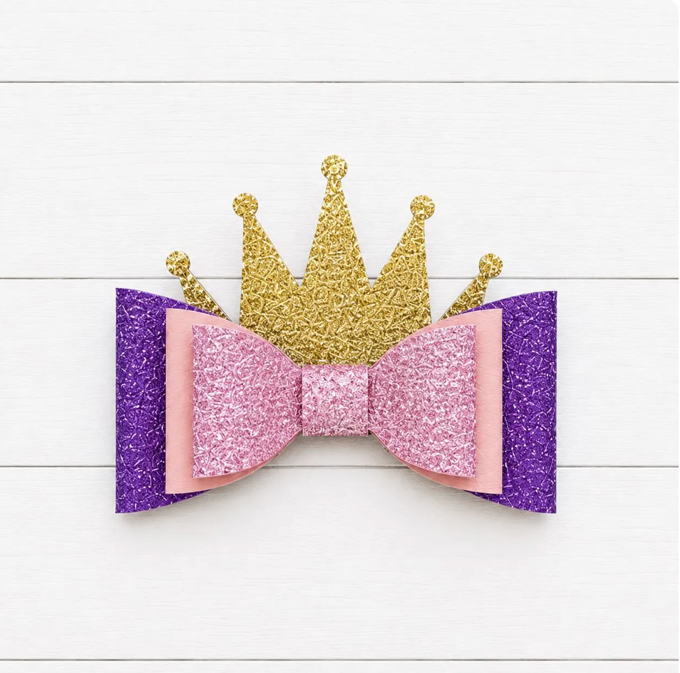 Glittery purple and pink bow with a gold crown on a white wooden background