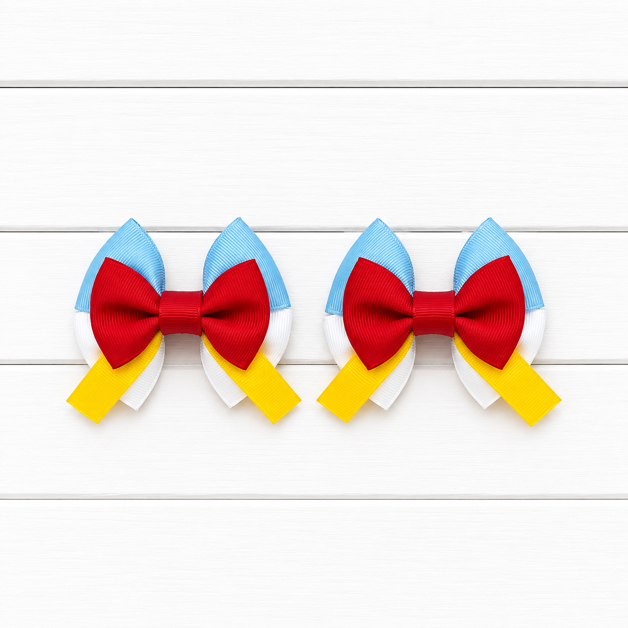 Two matching hair bows with light blue top, white bottom, red bow in the middle, and yellow tails