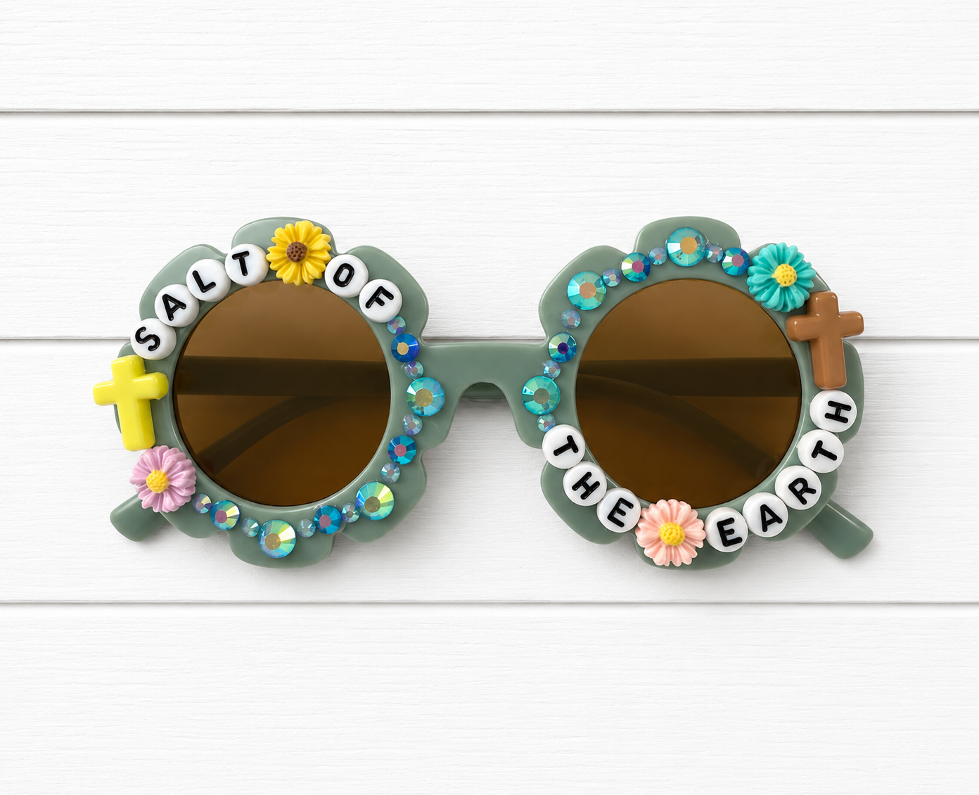 Kids green flower Sunglasses with rhinestone and floral outlined frame, yellow and brown cross charms, and text 'Salt of the Earth' surrounding the lens