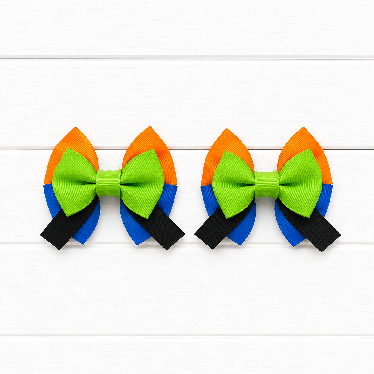 Two matching hair bows with orange top, blue bottom, green middle bow, and black tails