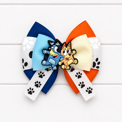 Blue and orange hair bow with Bluey and Bingo charm in the middle and paw print ribbon in the middle. 