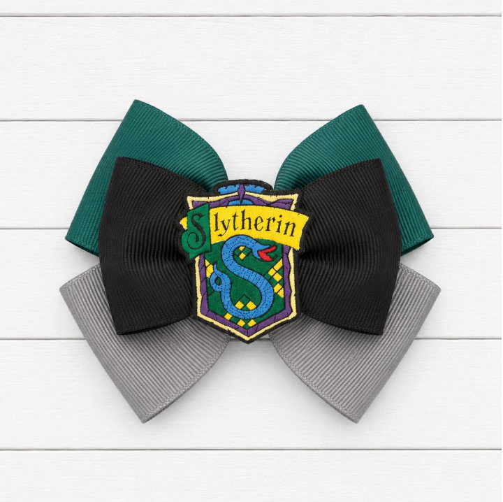 Green and grey bow with Slytherin emblem on a white wooden background
