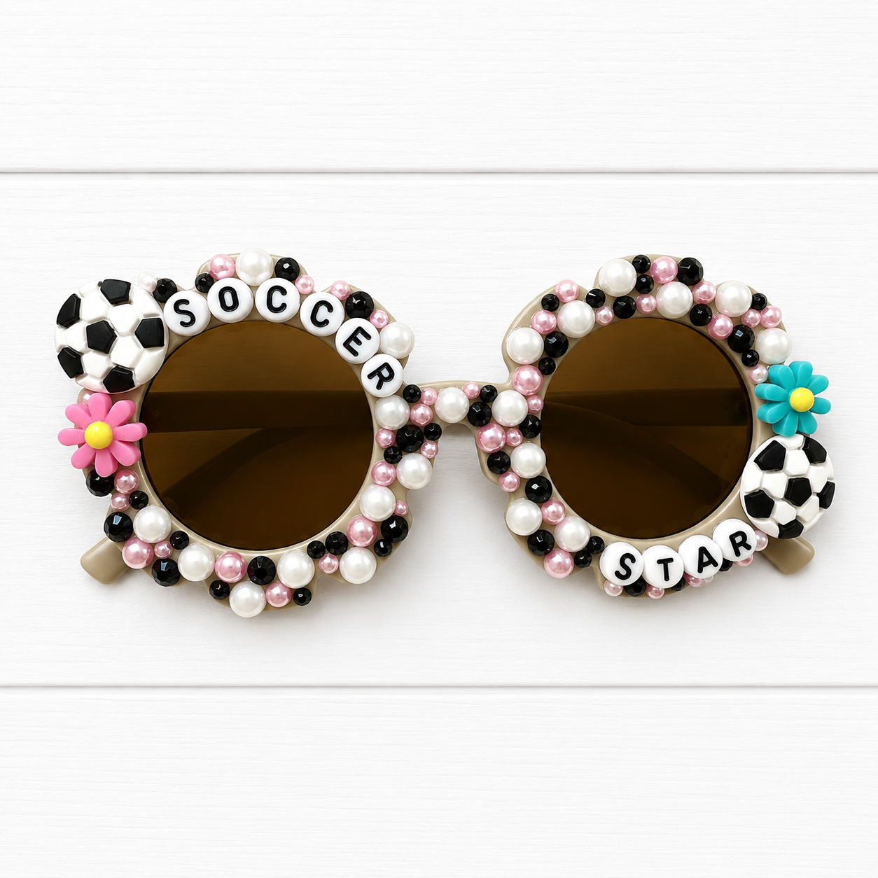 Kids grey flower sunglasses with "SOCCER STAR" text outlining frame and two soccer charms with two flowers and bedazzled with white, black, and pink rhinestones and pearls