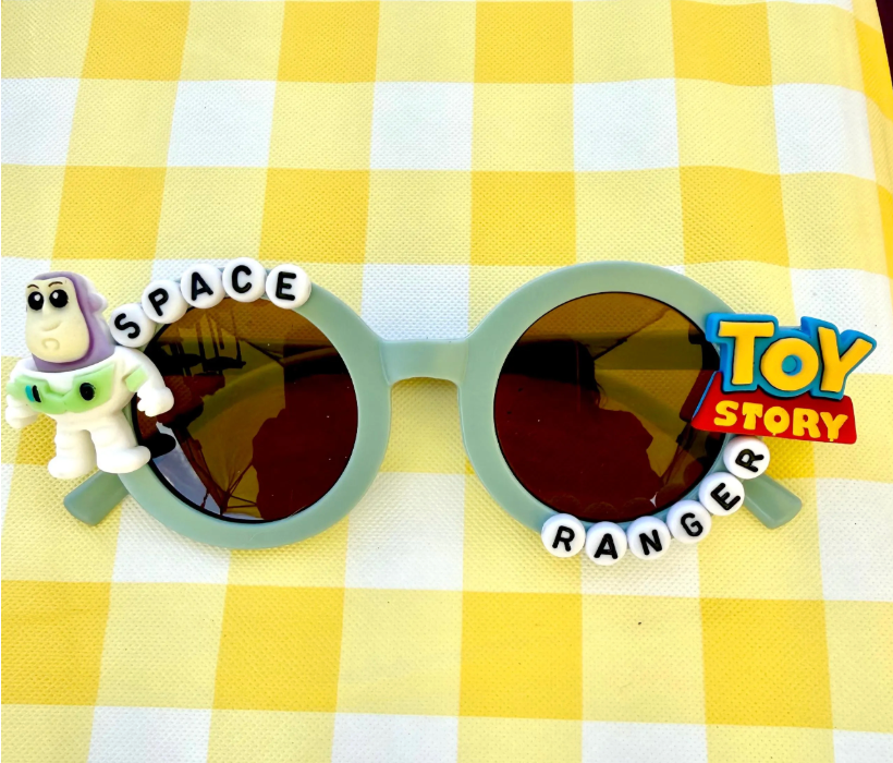 Kids light green round sunglasses with Buzz Lightyear charm on left side, Toy Story logo charm on right side, and "Space Ranger" text around the frames