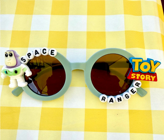 Kids light green round sunglasses with Buzz Lightyear charm on left side, Toy Story logo charm on right side, and "Space Ranger" text around the frames