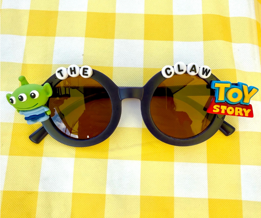 Kids round black sunglasses with little green alien on the left side from Toy Story and writing across the top that says "The Claw" with the Toy Story logo on the right side