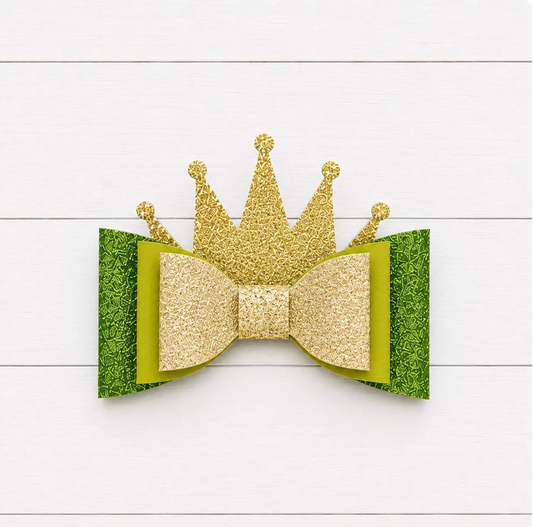 Gold glitter crown and green bow on a white wooden background