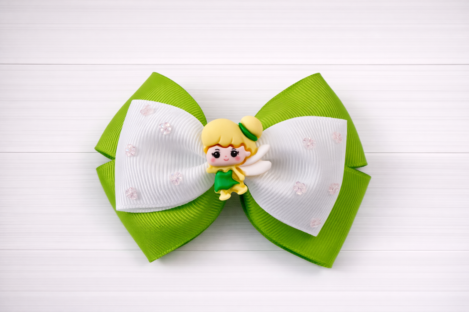 Green and white hair bow with a Tinkerbell charm in the middle on a white wooden background