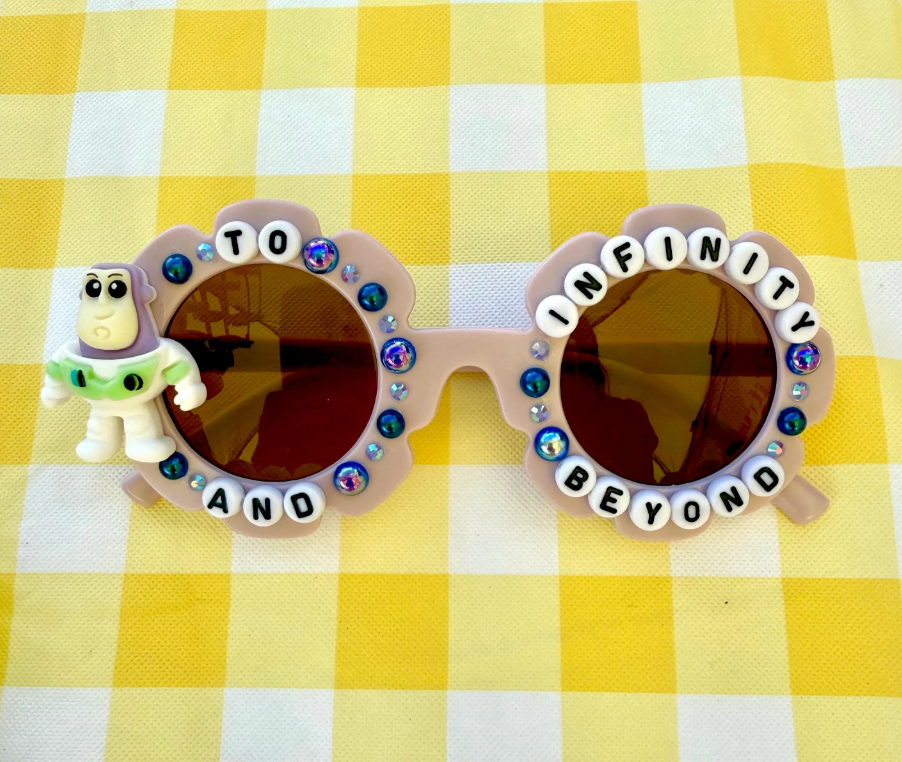 Kids purple sunglasses with Buzz Lightyear character and the text "To Inifinity and Beyond" with purple rhinestone detailings around the sunglasses