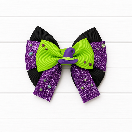 A Halloween-themed hair bow featuring black grosgrain ribbon loops, purple glitter panels with small rhinestones, a bright lime green center loop, and a small purple witch hat accent on a white wood plank background.