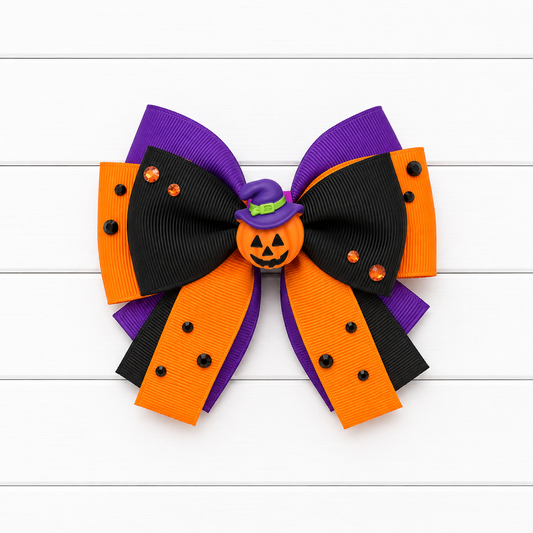A Halloween-themed hair bow made of purple, black, and orange grosgrain ribbon, featuring a small jack-o'-lantern ornament in the center with a purple witch hat and orange rhinestones, displayed on a white wood plank background.